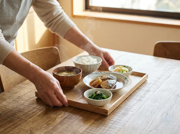 トレーに乗った和食の昼食をテーブルに置く職員の手元